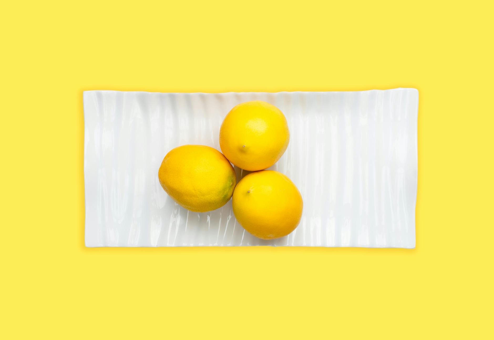 Fresh lemons arranged on a white plate with vibrant yellow background, symbolizing vitality and calm