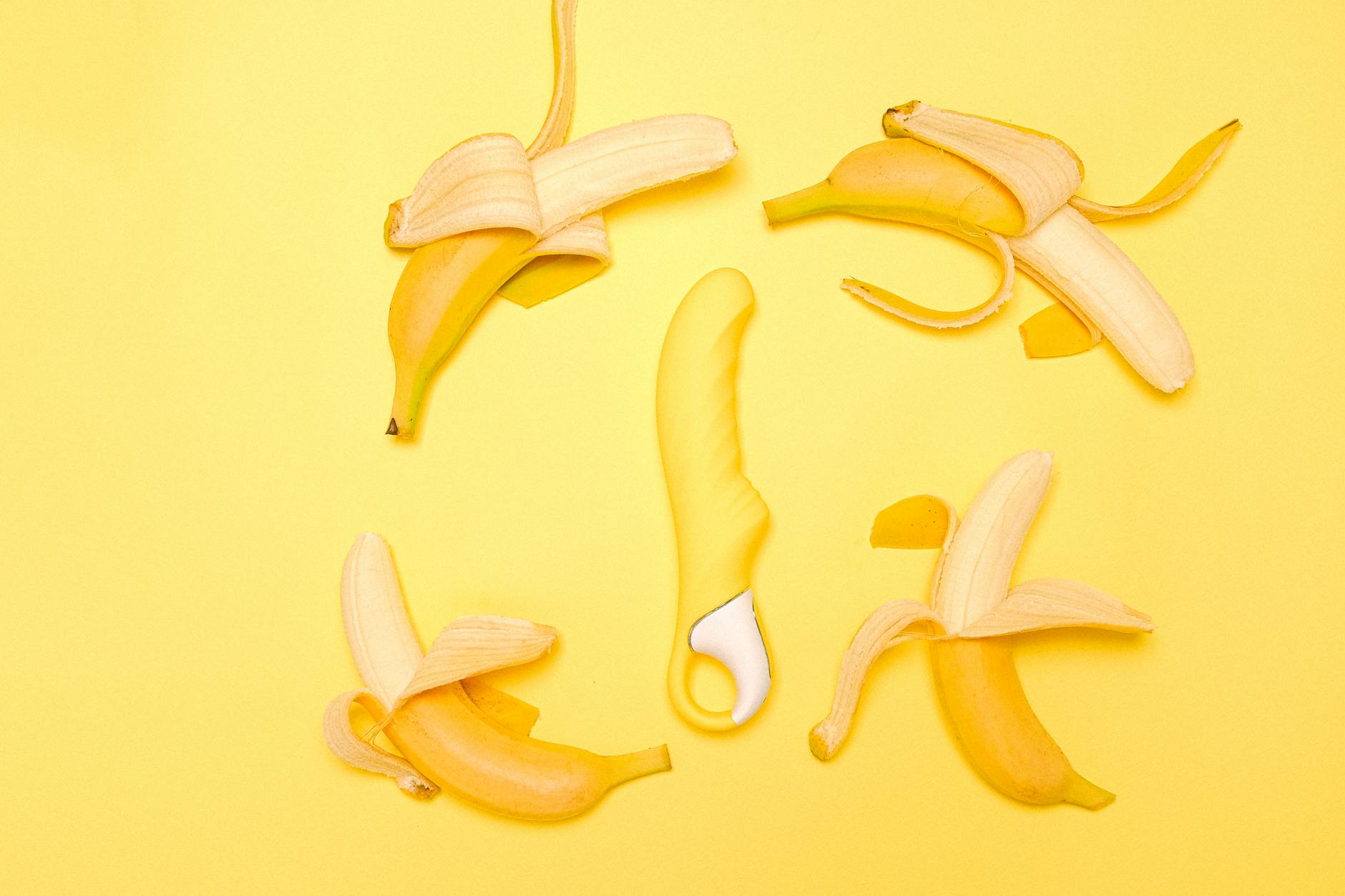 Diverse collection of colorful vibrators and adult toys arranged on a bright yellow surface.